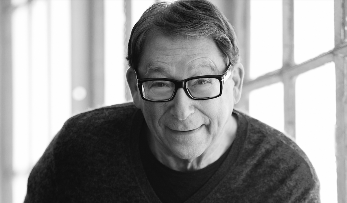 Black-and-white portrait of Stuart Weitzman wearing glasses and a dark sweater. He is smiling.